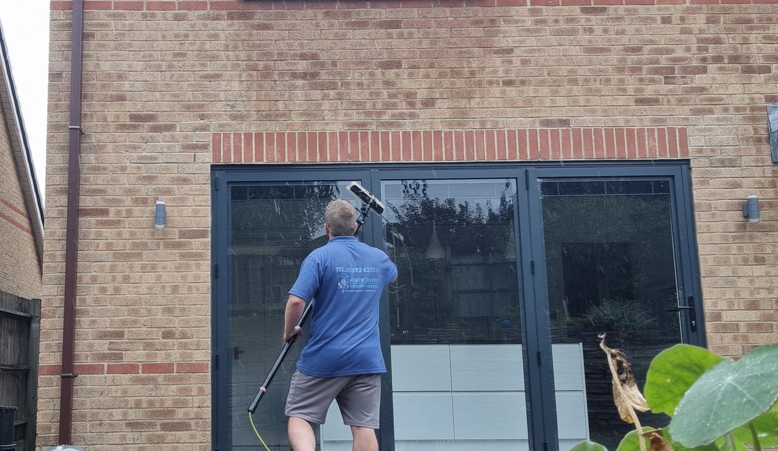About Us 7 An image of a guy cleaning glass doors with a water-fed pole