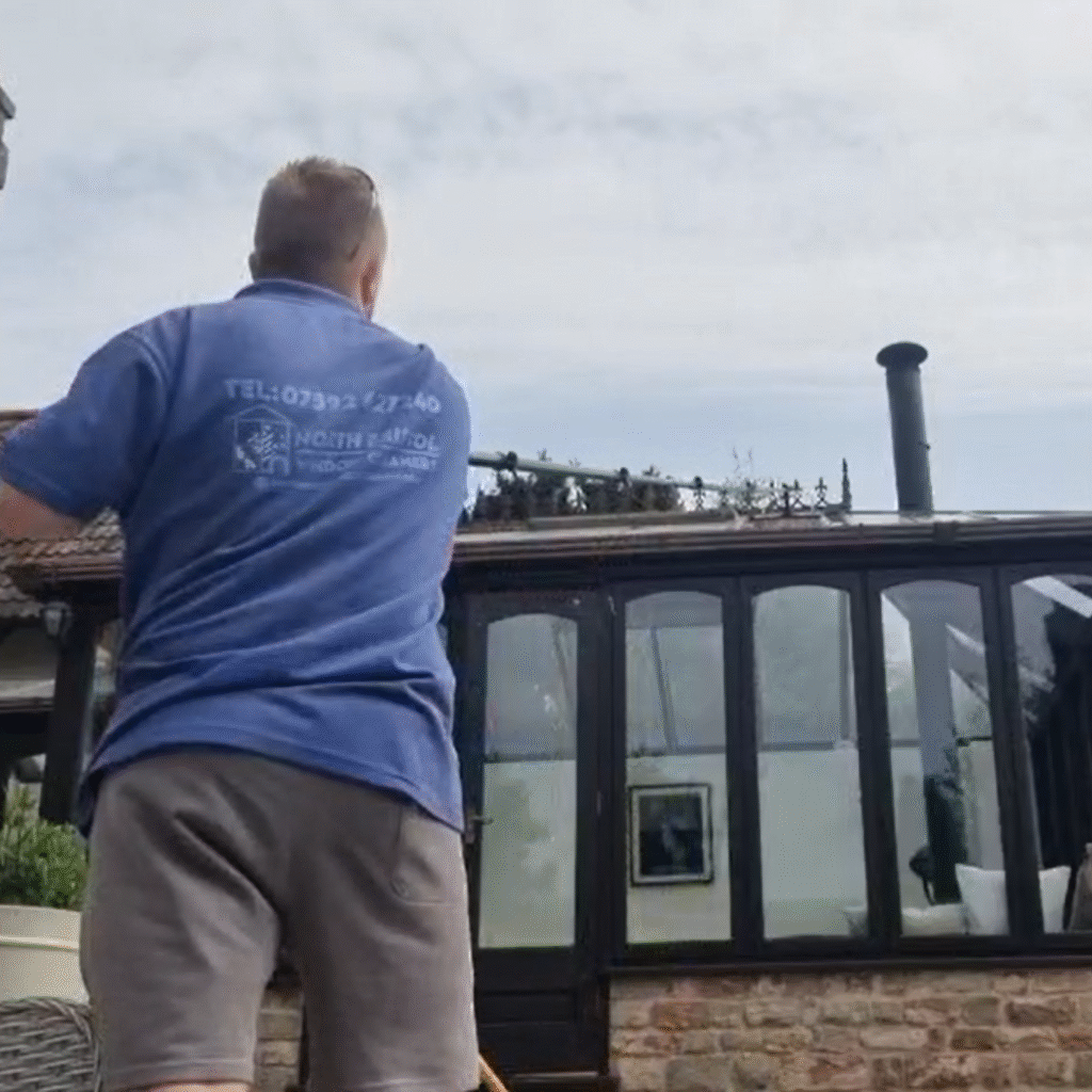 An image of a man on blue polo shirt cleaning windows and conservatory roof with a water-fed pole