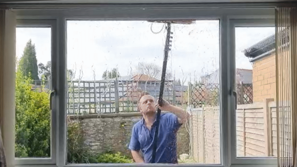 an image of a guy with a blue polo shirt cleaning a residential window with a water-fed pole
